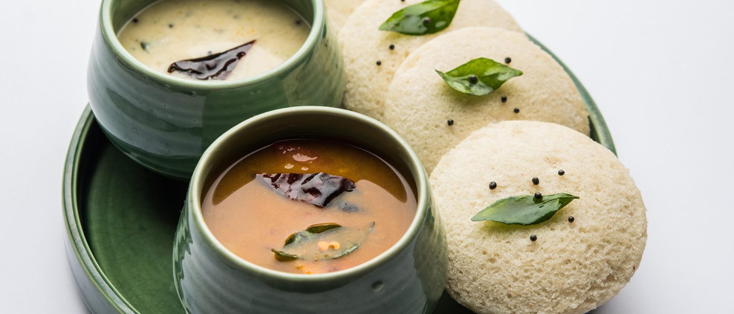 Close-up of four idli with two different sauces in small pots.