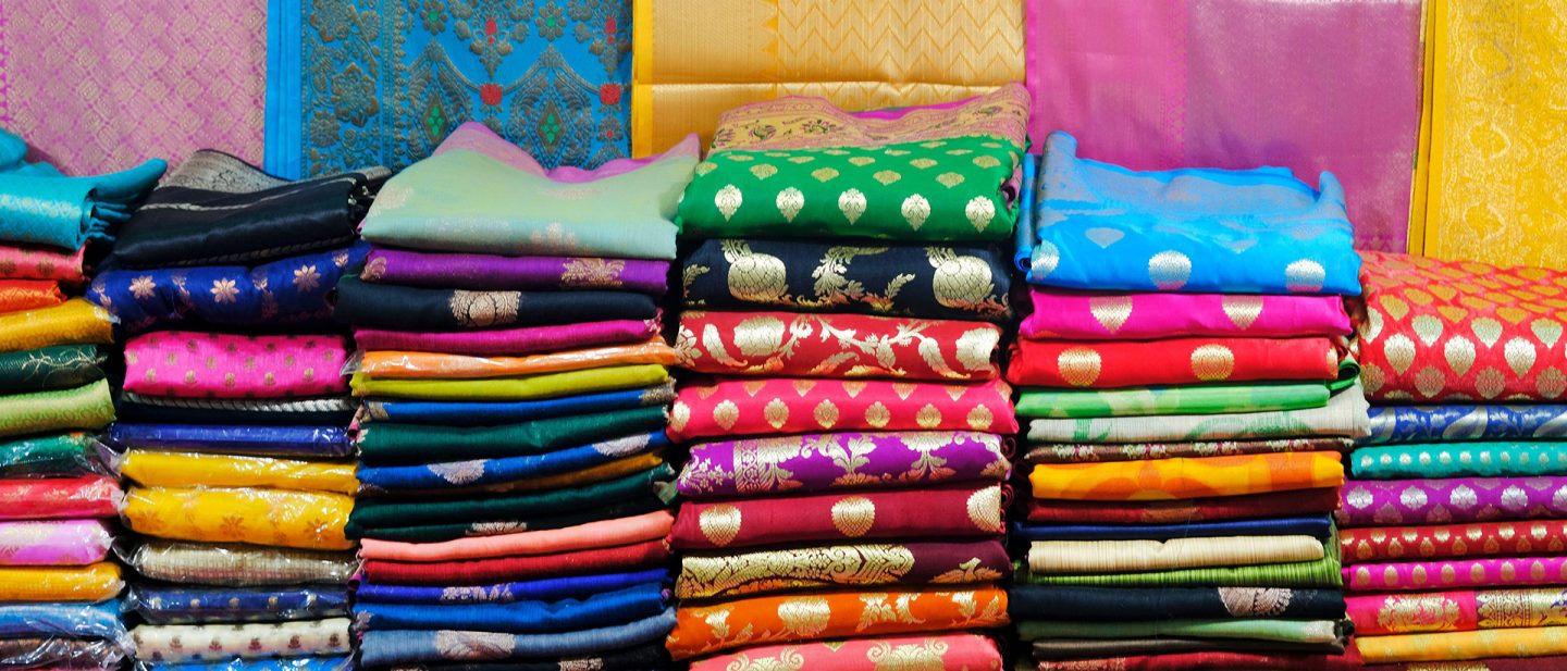 Picture of many colorful sari fabrics, folded and stacked.
