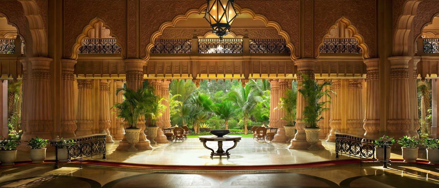 View of a palm garden through the archways of The Leela Palace hotel