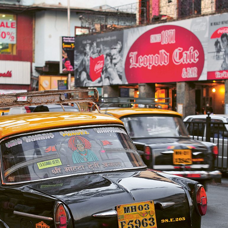 Facade of the Leopold Cafe in the background, a street with cabs in the foreground