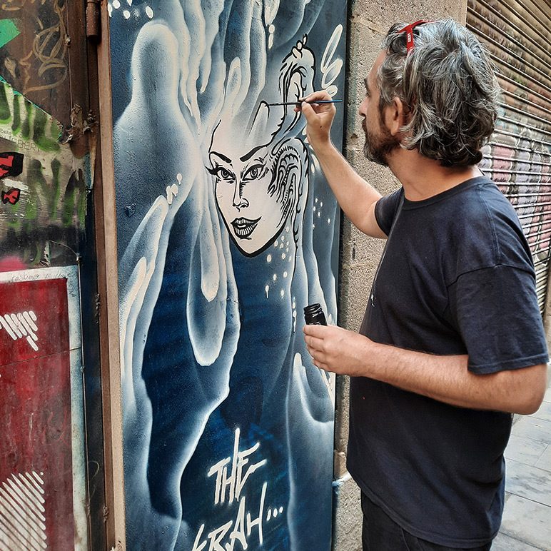 Artist The Krah holding a paintbrush in front of a picture