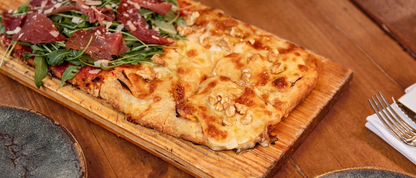 Pizza with cream cheese, apple, nuts, and honey on a wooden board at a pizzeria in Barcelona