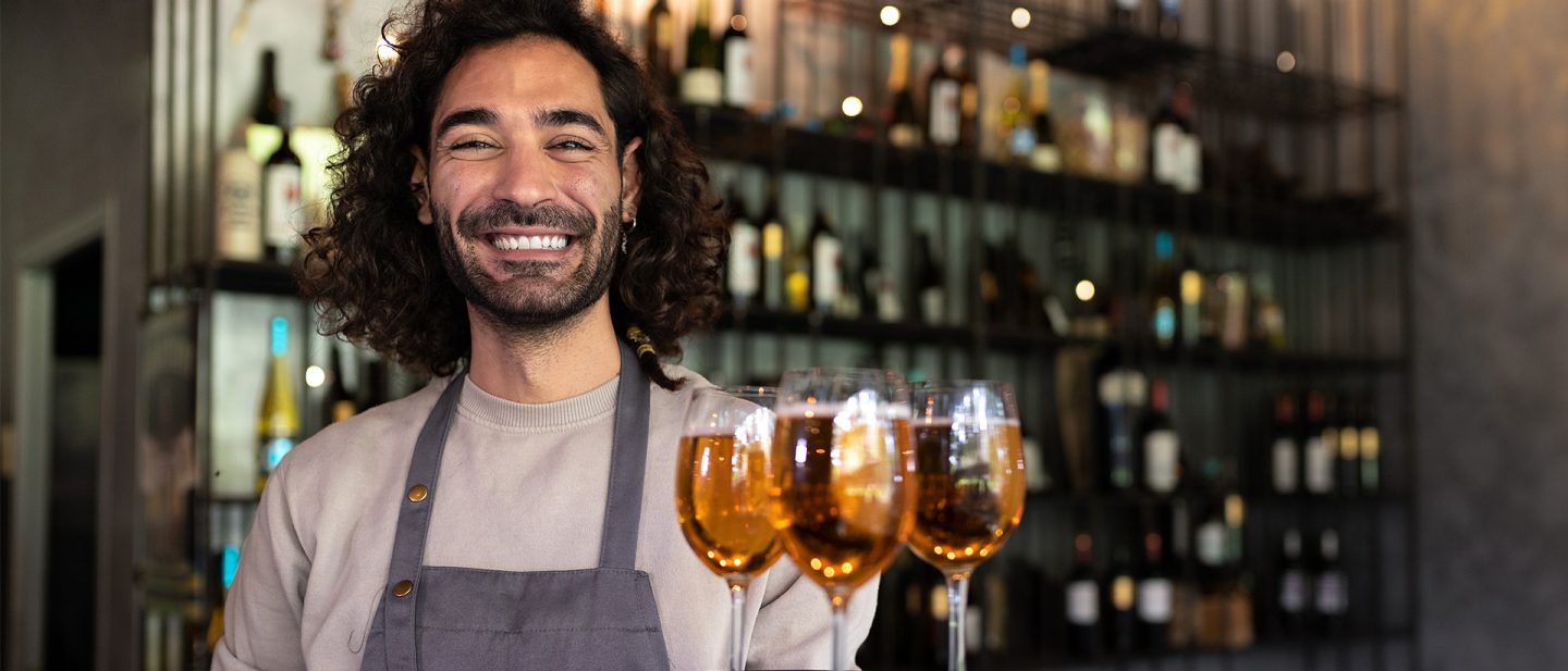 Waiter smiles at the camera and holds a tray with three glasses of beer.