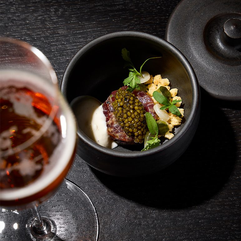 Nobly served fish sushi with caviar on top and beer glass next to it and chopsticks.