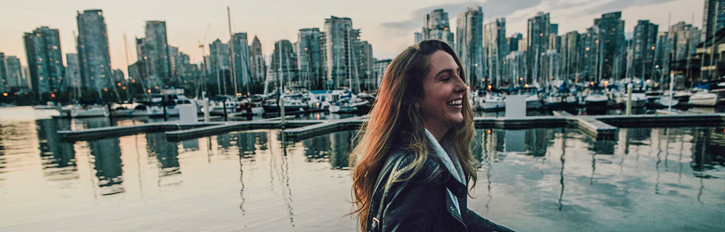 Woman with long hair stands laughing at the harbor of Vancouver, in the background: water and the skyline