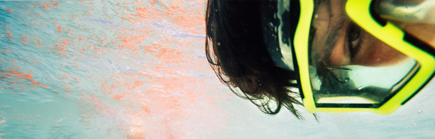 Close-up of a diver with yellow diving goggles, you can mainly see his eyes, in the background water