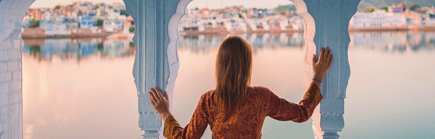 Woman in patterned top looking at a waterfront cityscape through arched window.