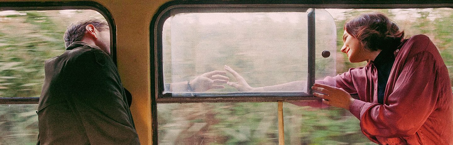 A man and a woman on a train shake hands through an open window.