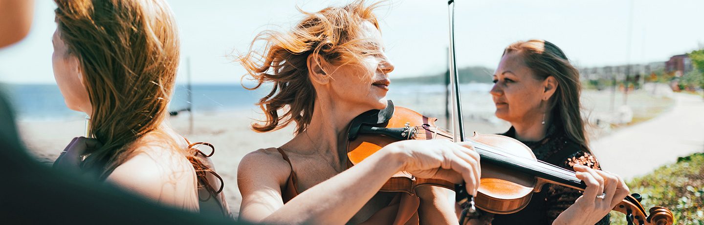  A woman plays violin outdoors, surrounded by people, with wind in her hair by the sea
