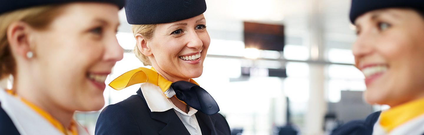Three Lufthansa flight attendants smiling in an airport terminal