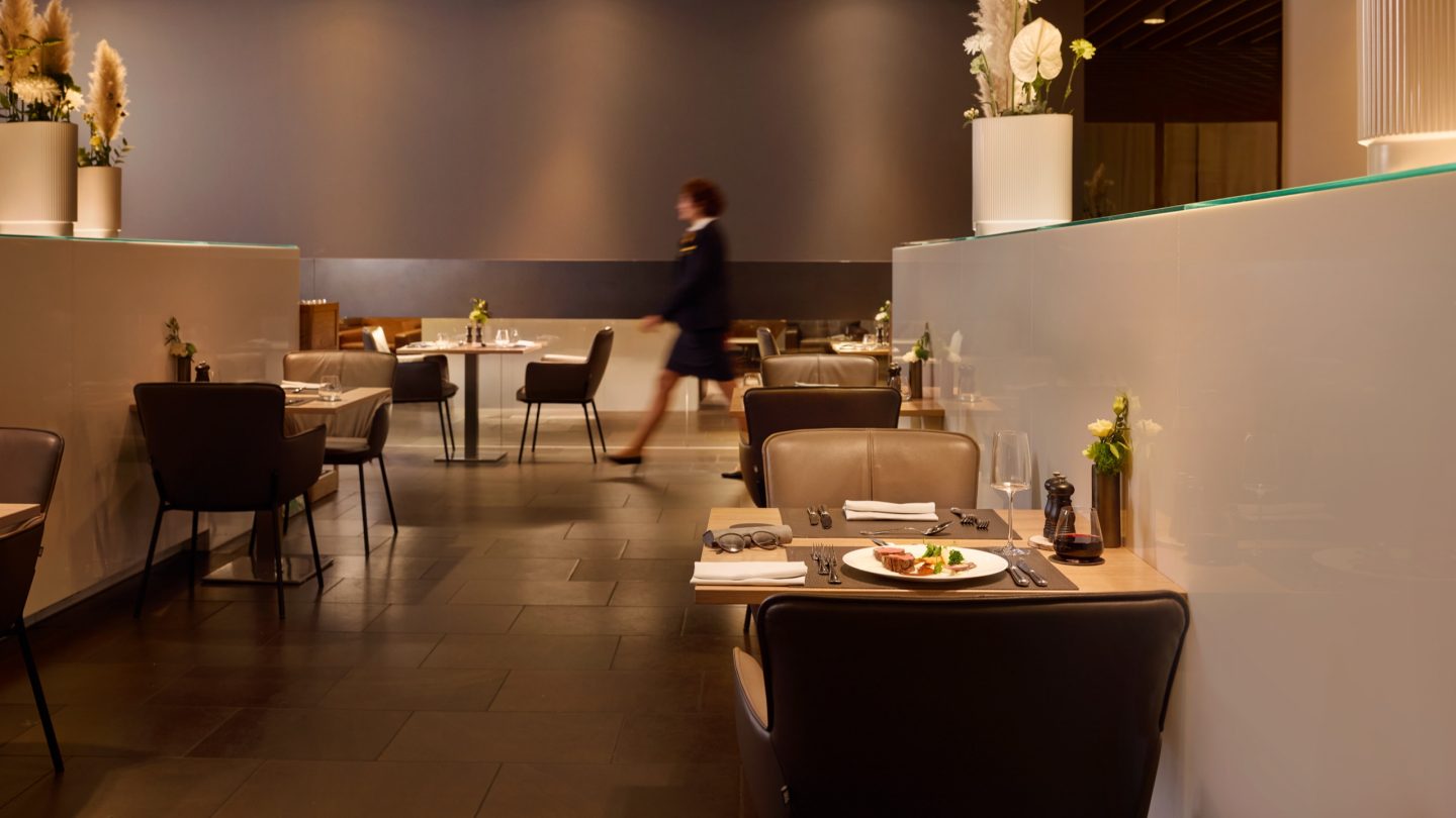Modern, sunlit airport lounge seating area with comfortable armchairs.