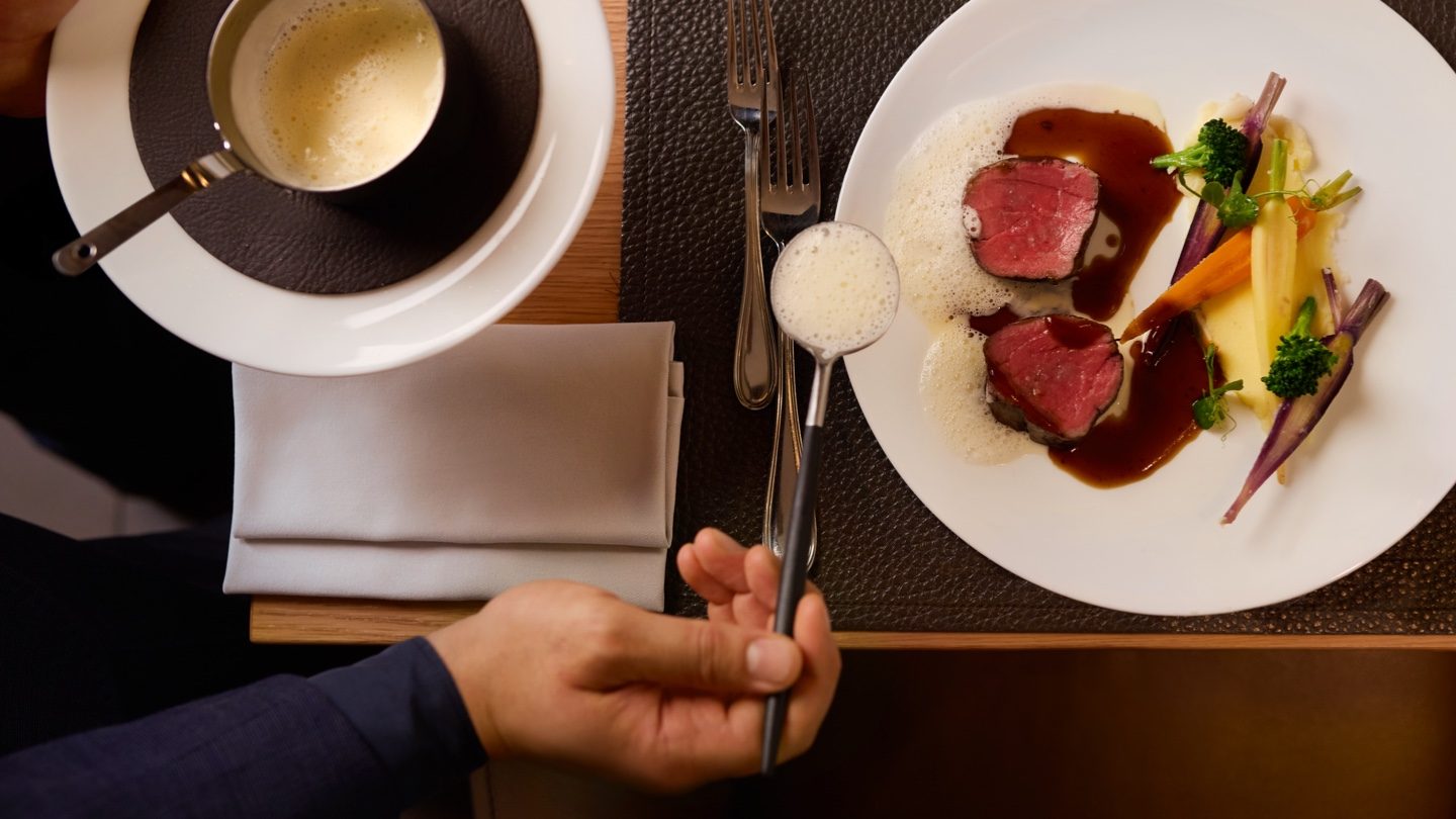 Gourmet beef medallions and vegetables on a plate with a foamy drink.