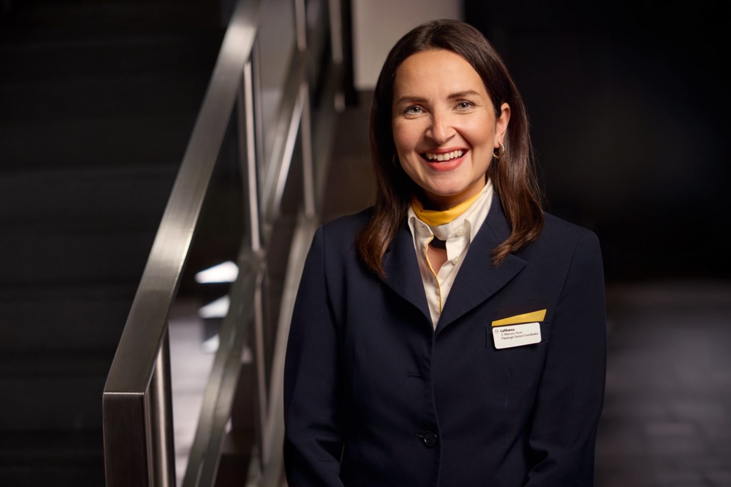 Professional woman in a navy blazer and yellow scarf by a staircase.
