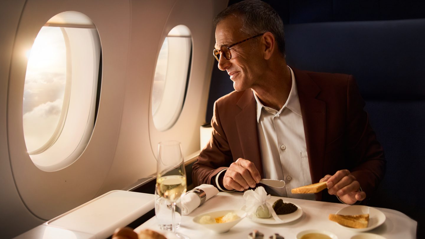 A man in a suit enjoys a gourmet meal with champagne on a plane. 