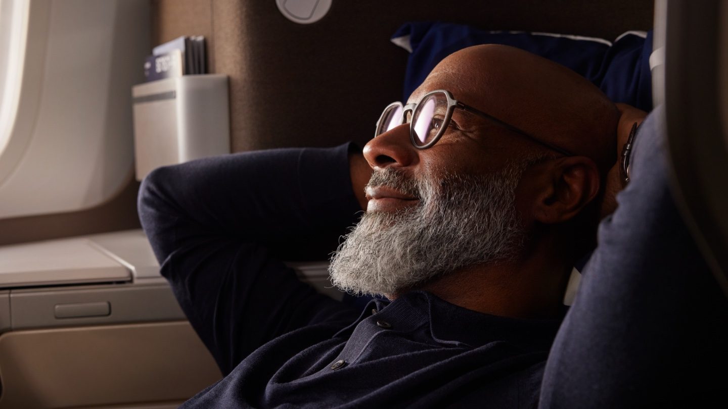 Bearded man with glasses relaxing by an airplane window.