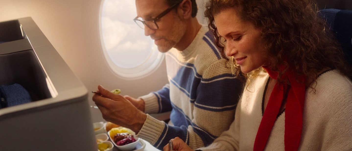 Two passengers enjoying a meal on an airplane.