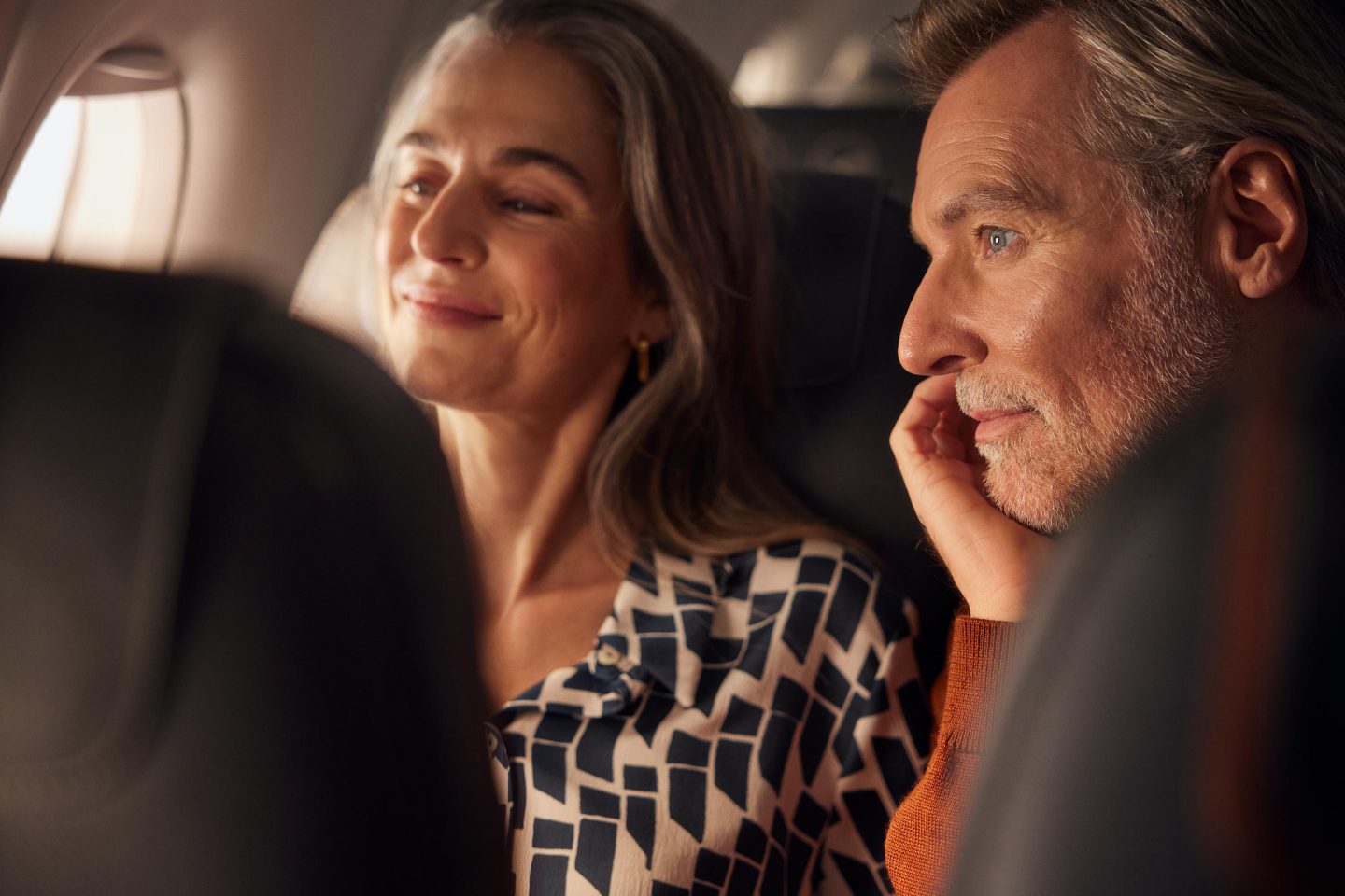 Finally, the journey begins: two older travellers look out of the aircraft window, full of anticipation.