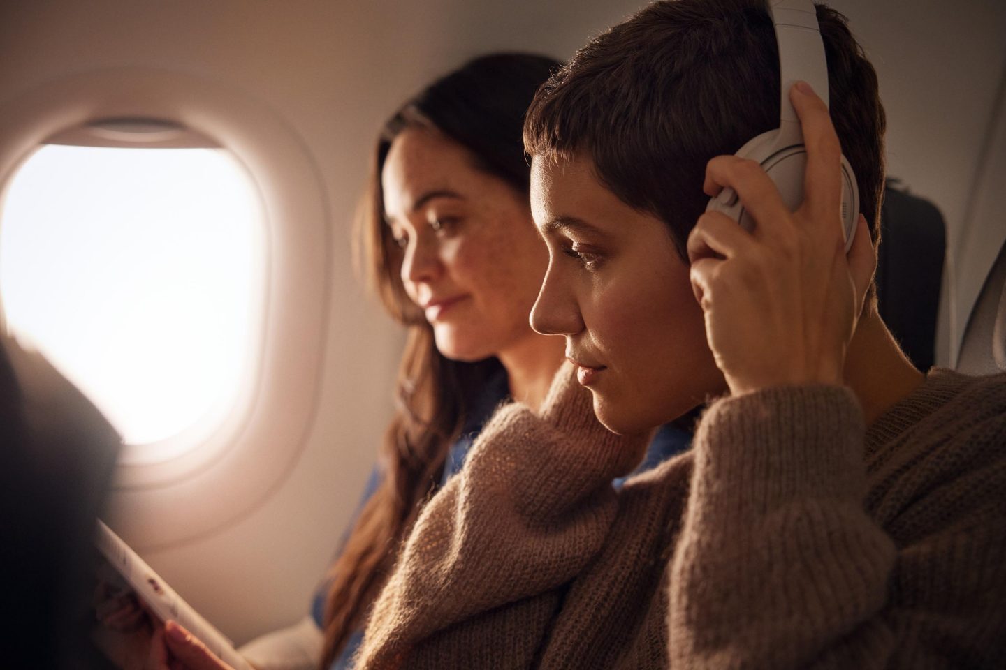 Two women wearing headphones relax with a book in the aircraft.