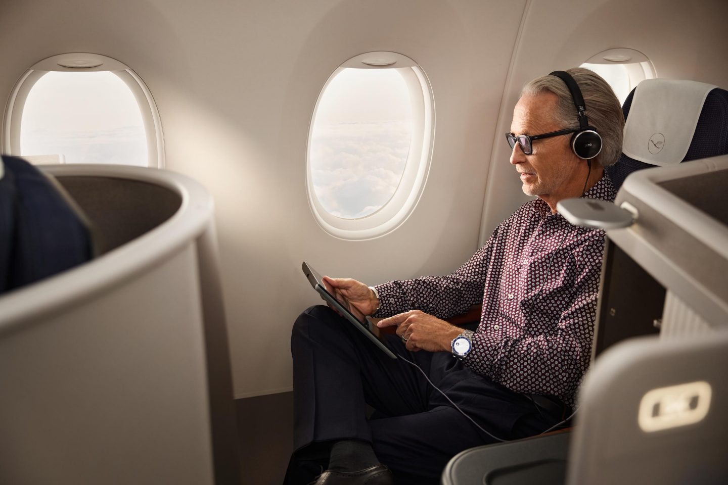 Ein Gesch&auml;ftsmann sitzt im Allegris Business Class Privacy Seat und h&auml;lt ein Tablet in der Hand. // A businessman sits in Allegri's Business Class Privacy Seat holding a tablet.