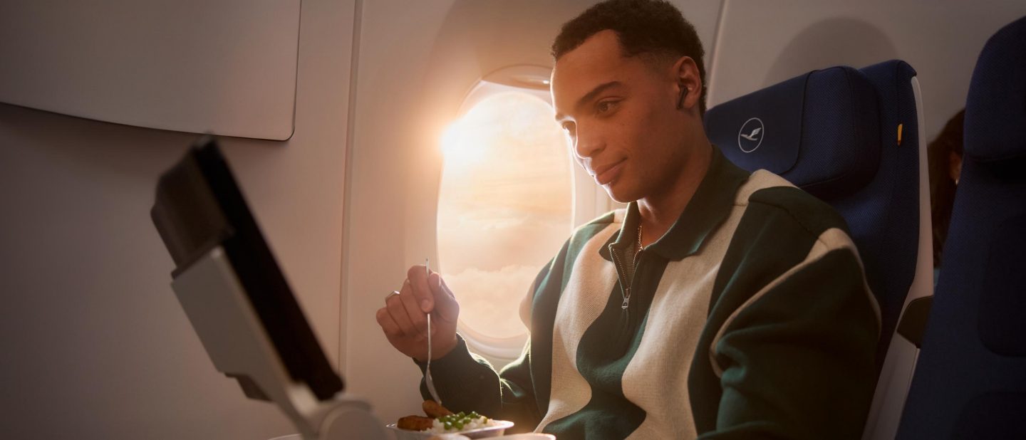 Passenger enjoys an airline meal by a sunlit window on a flight.