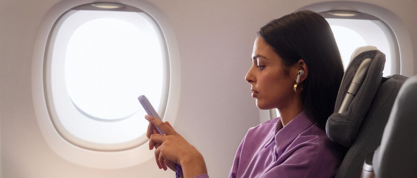 A young woman sits in Business Class on the A380 and looks at her smartphone.