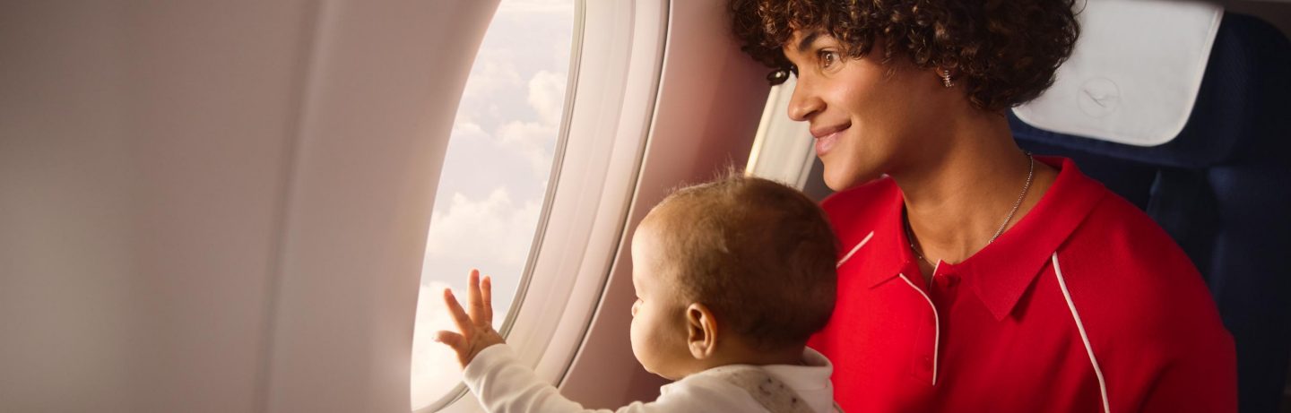 Mom and baby look out airplane window, enjoying the clouds.