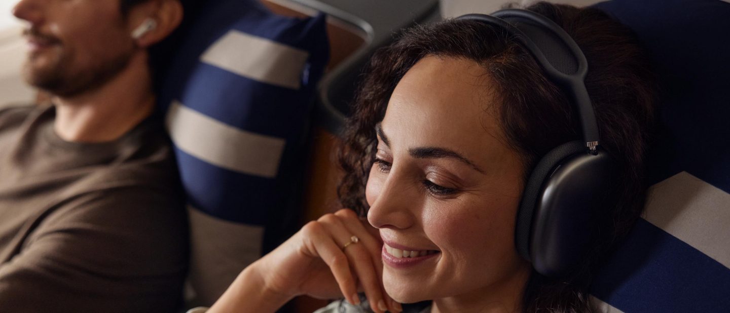 Smiling woman with headphones enjoys a relaxed flight. Man in background.