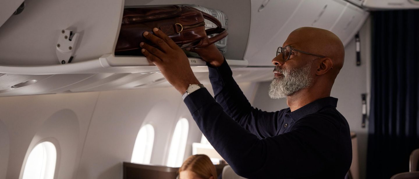 Mann verstaut sein Gep&radic;&sect;ck &radic;&ordm;ber dem Sitz an Bord. // Man stowing his luggage over the seat on board.