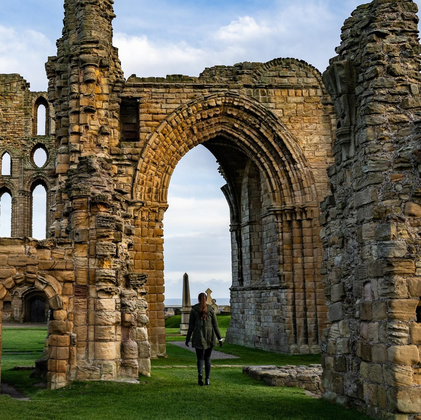 Person walking through historic abbey ruins with a large Gothic arch.