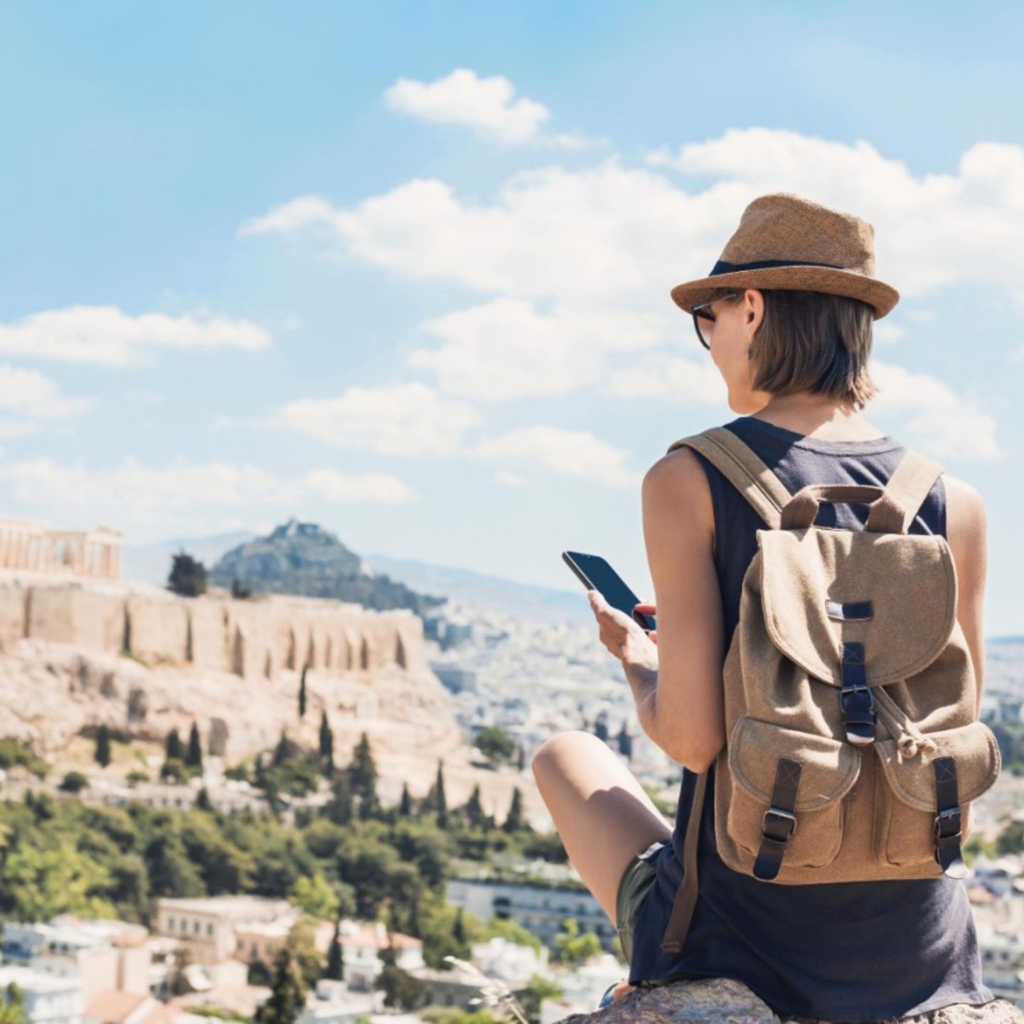 Tourist with backpack and phone enjoys Parthenon & Athens panorama.