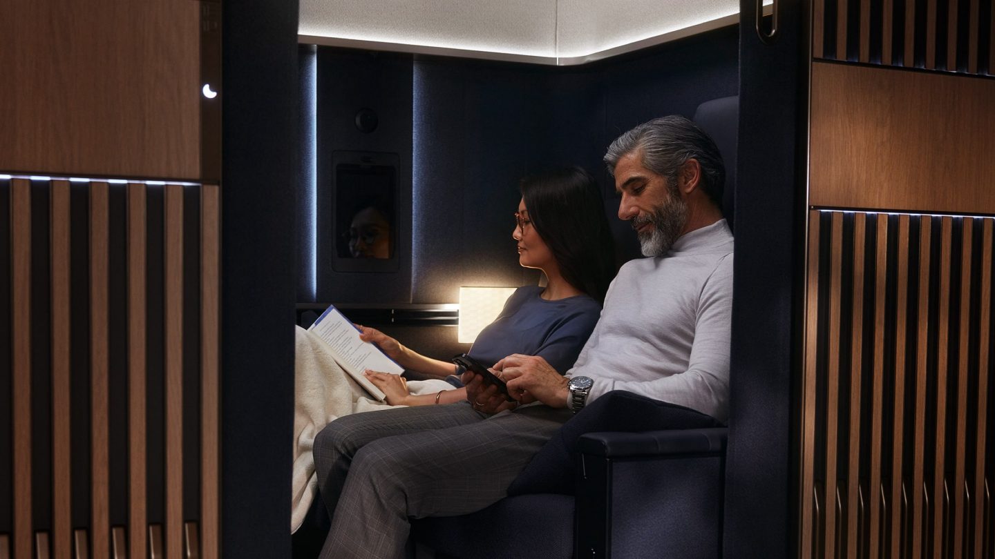 A couple relaxes in a luxurious airline first-class suite with wood paneling.