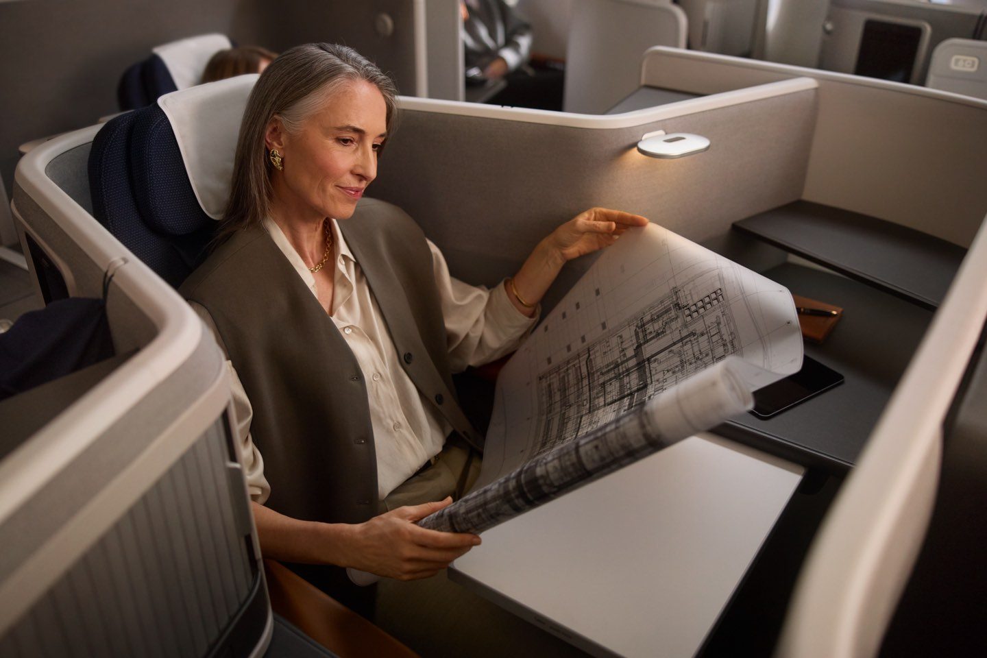 A woman reviewing architectural blueprints while seated in an airline business class cabin.