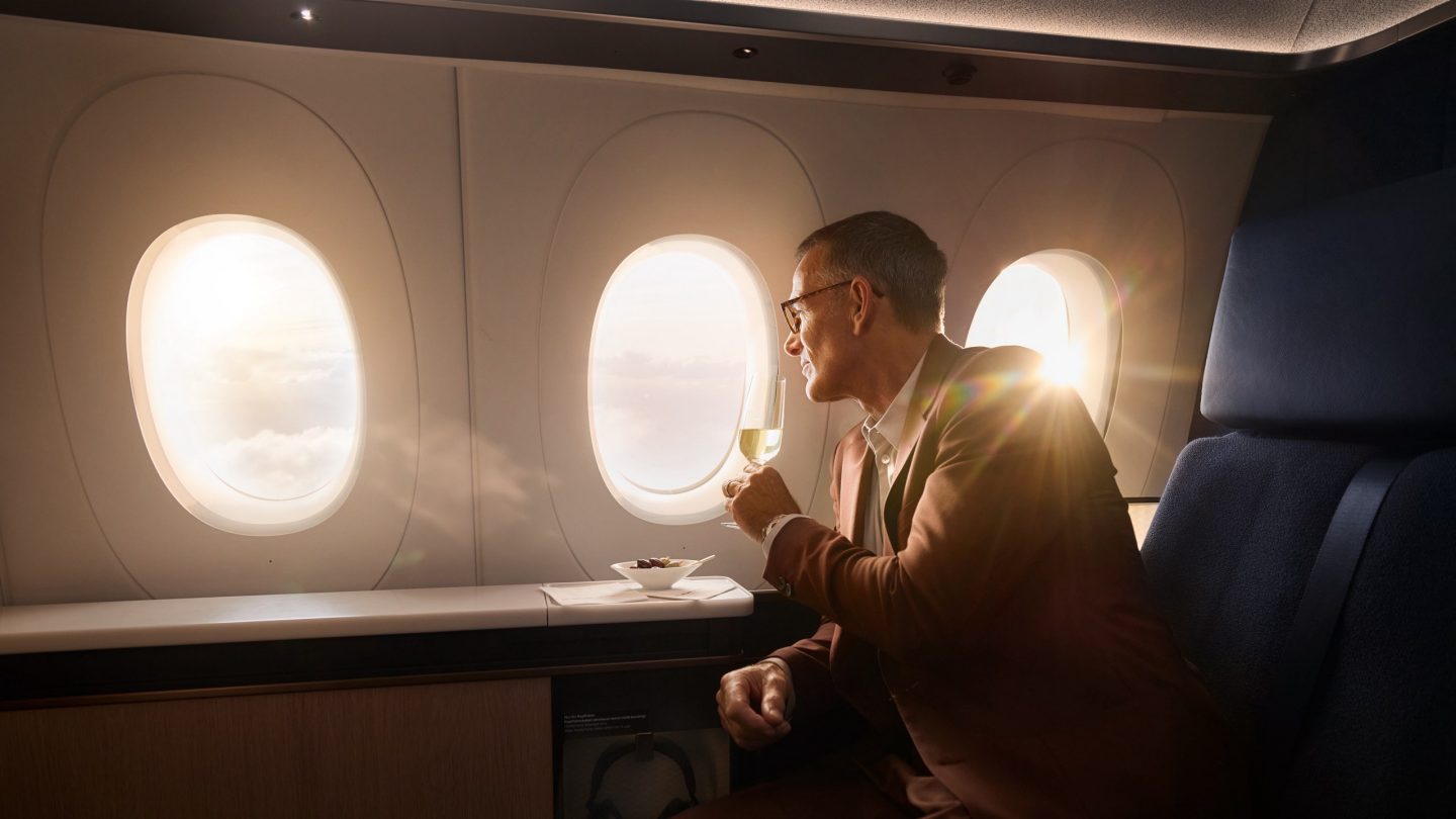 Man sips champagne, admiring the bright sky view from his premium airplane seat.