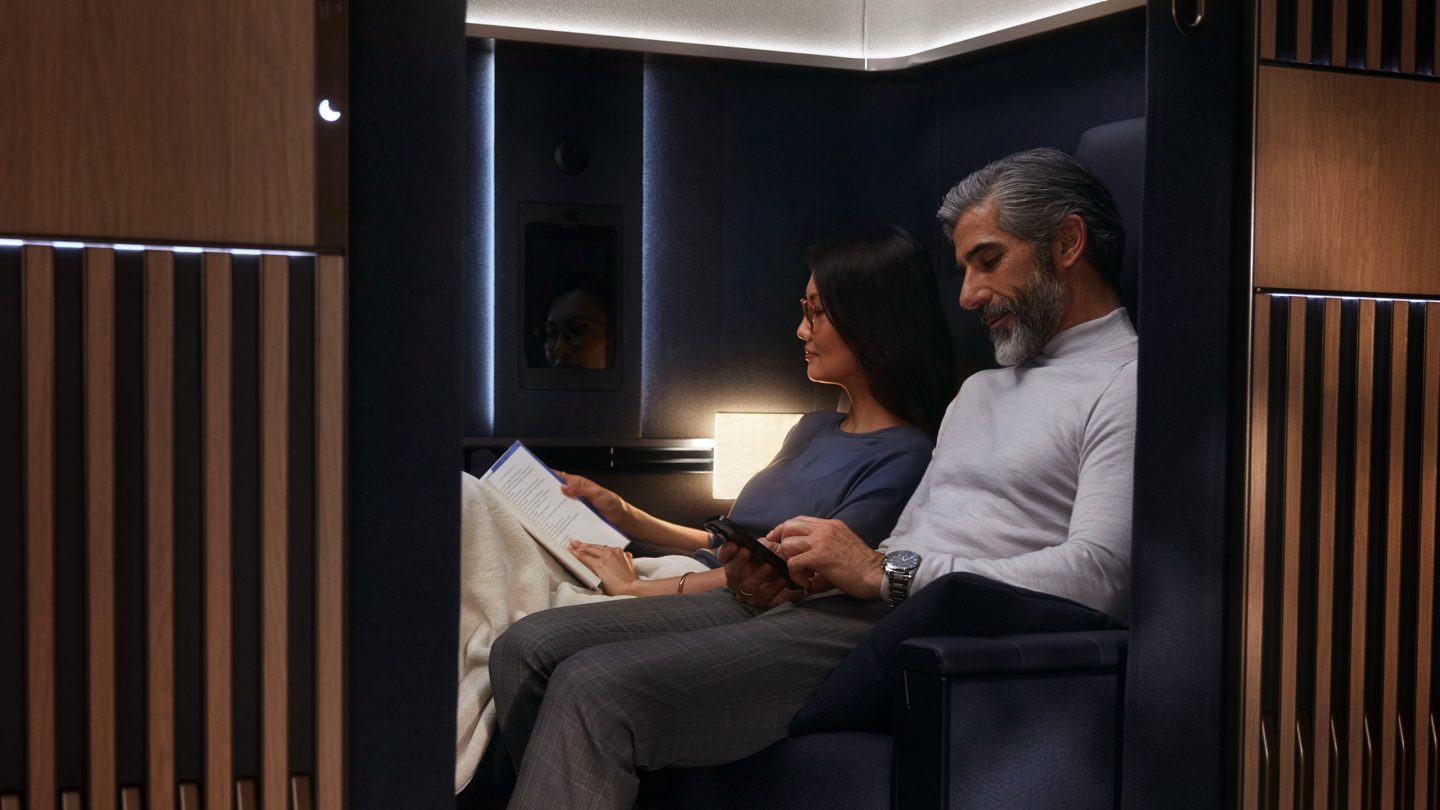 Passengers relax in a modern, private airline suite, reading and using phone.