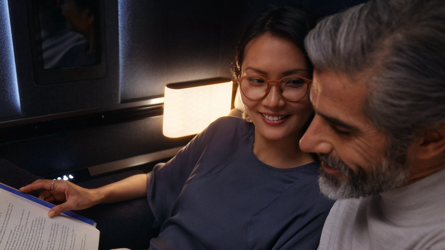 Two passengers enjoying a book together in a premium airline cabin.