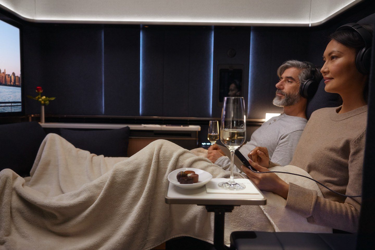 Couple relaxes in a luxury airline suite, enjoying entertainment, champagne, and comfort.