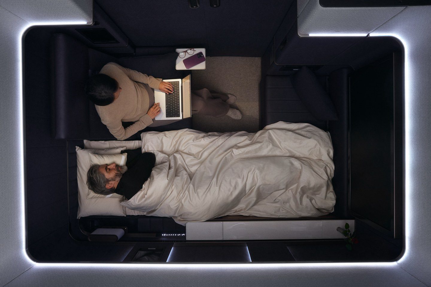 Private airline suite with one sleeping, one working on a laptop.