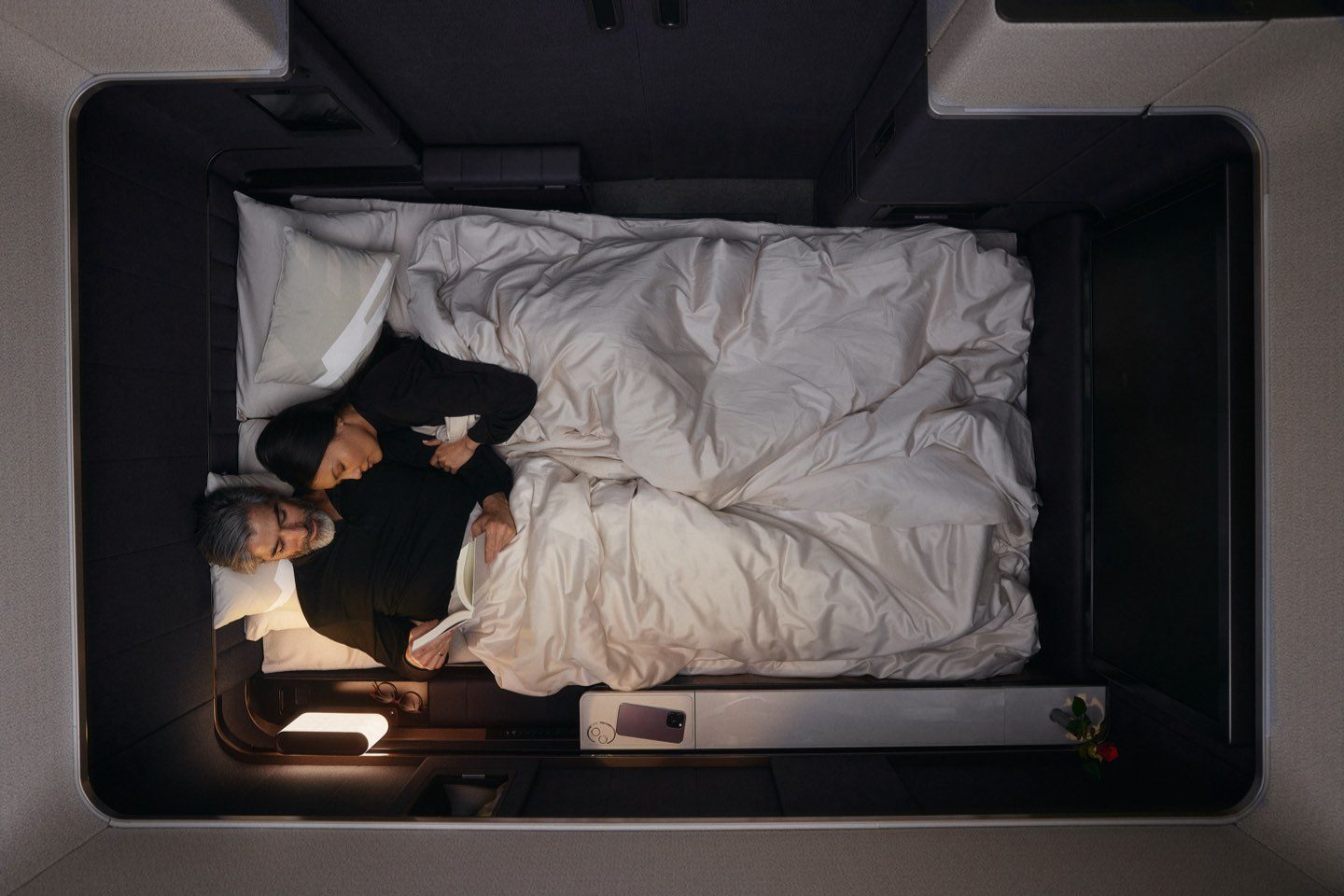 A couple sleeps peacefully in a luxurious airline suite bed.