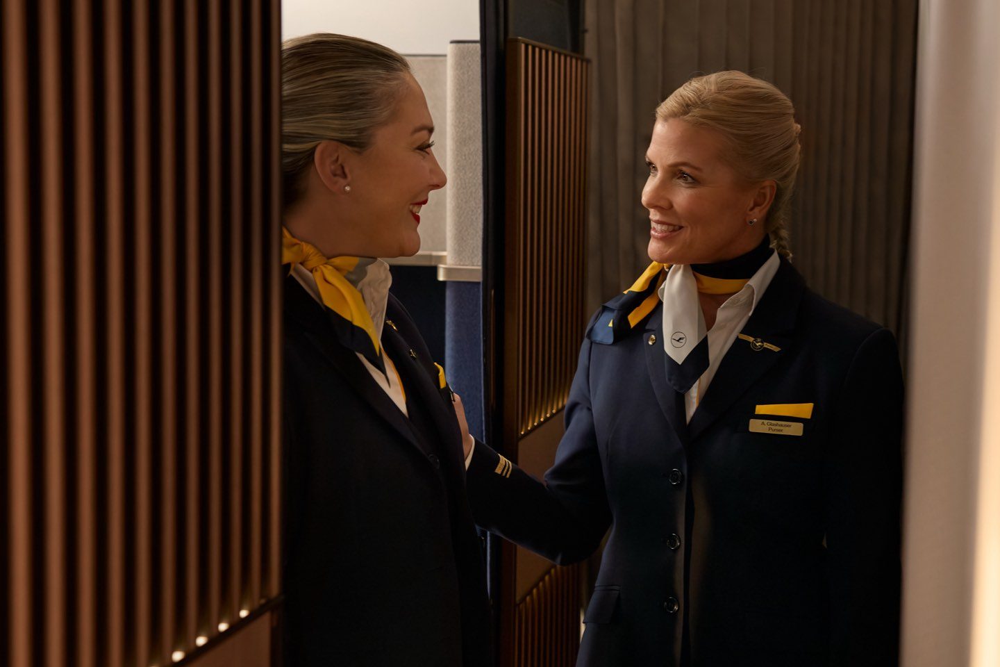 Smiling Lufthansa flight attendants sharing a friendly moment onboard.