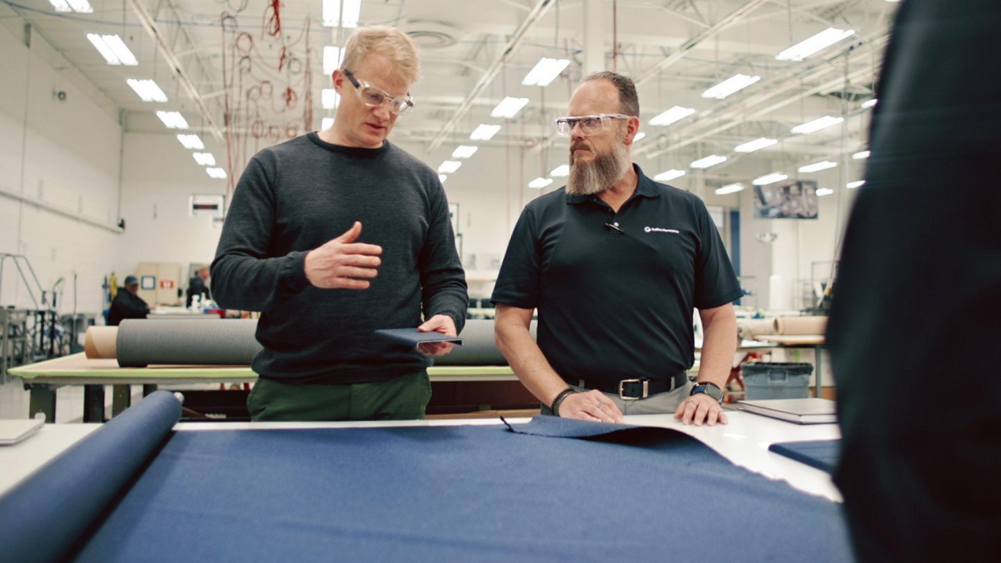 Man from Collins Aerospace & partner in safety glasses examining blue fabric.