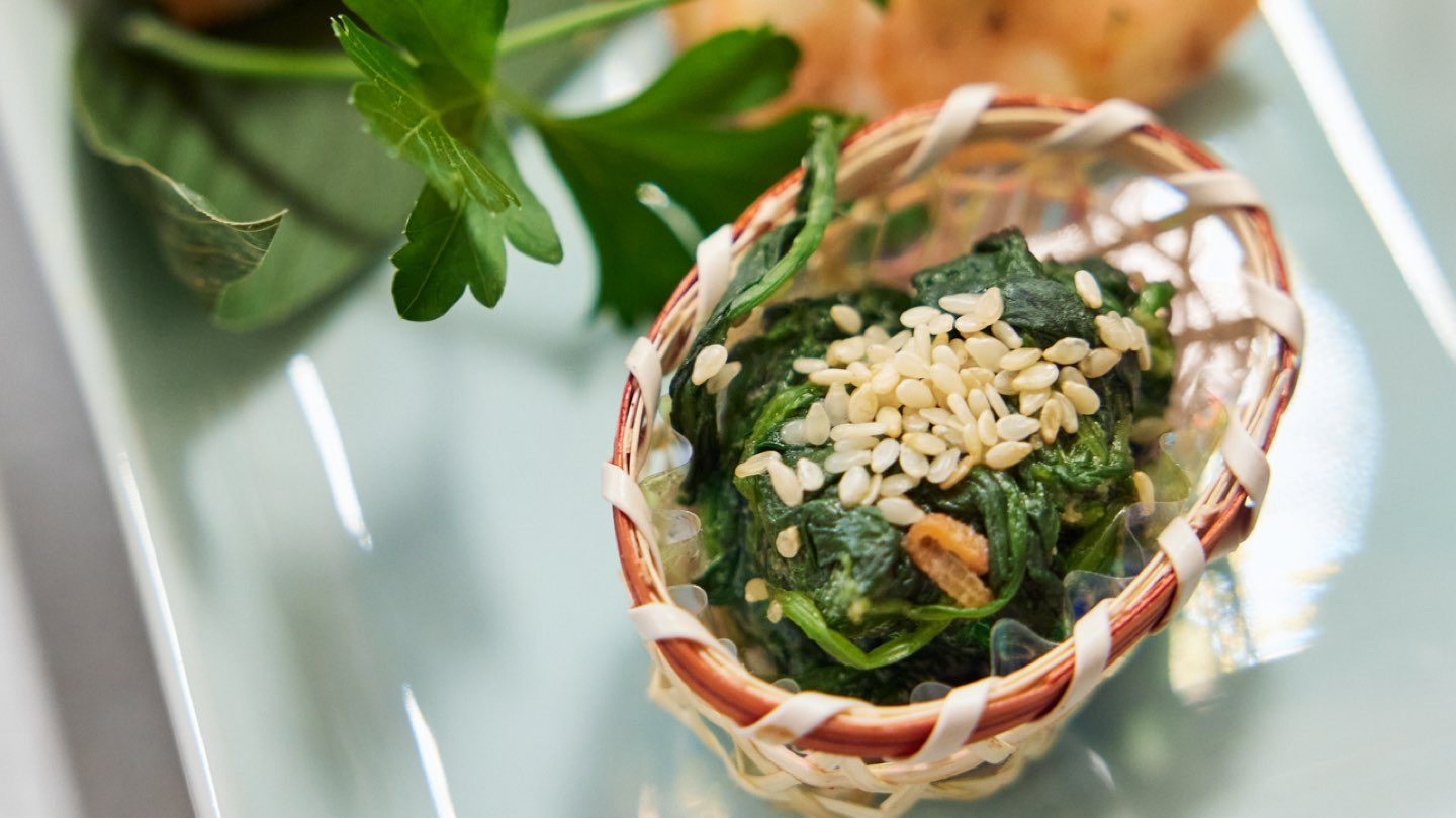 A small basket containing spinach topped with sesame seeds.
