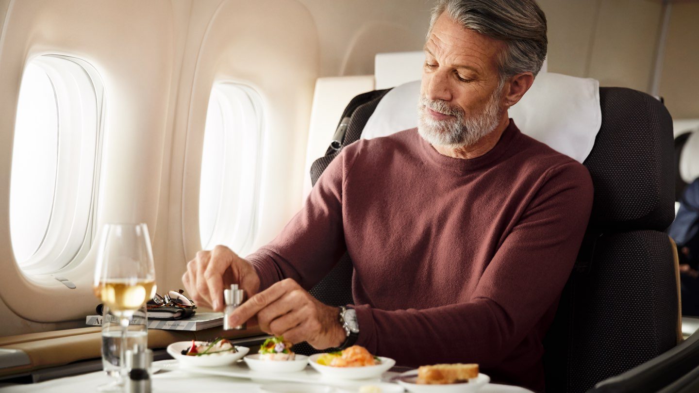 A man in an airplane seat, having a meal from a food tray.
