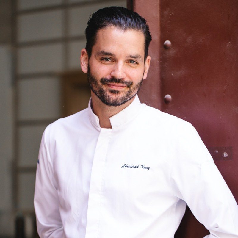 Star Chef Christoph Kunz poses in a white shirt in front of a door.