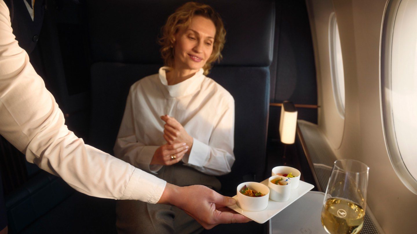 A woman in an airplane enjoys a tray of food, inviting exploration of diverse tastes through multiple courses.