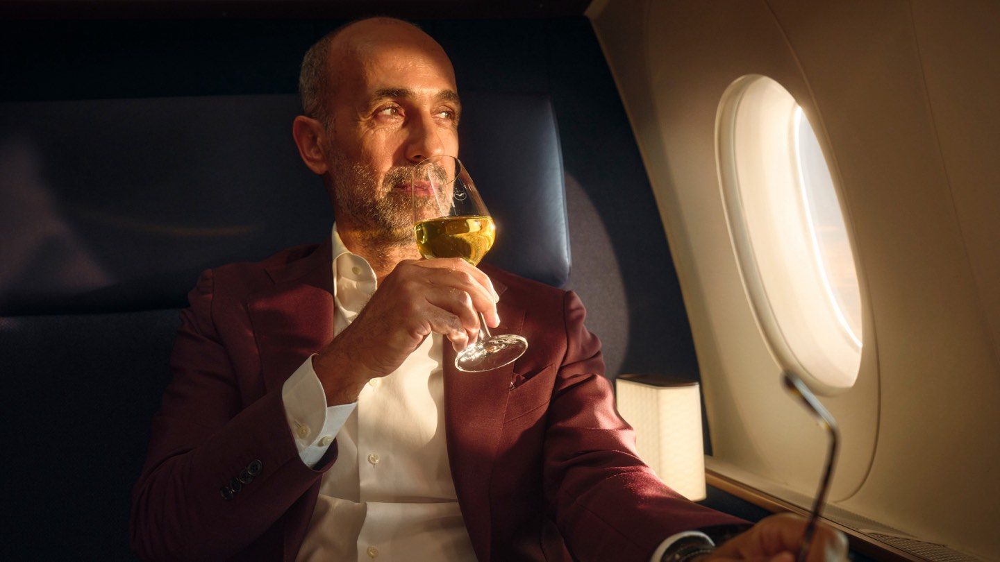 A man in a suit enjoys a glass of wine while seated on an airplane, showcasing world-class wines in-flight.