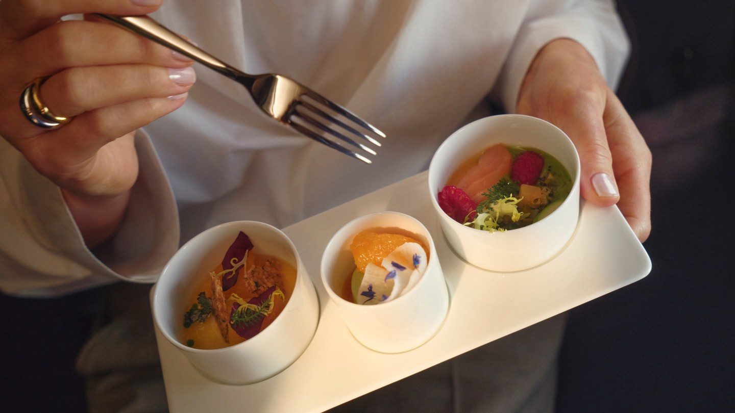 Person holding a fork and a tray with three small, artfully presented dishes.