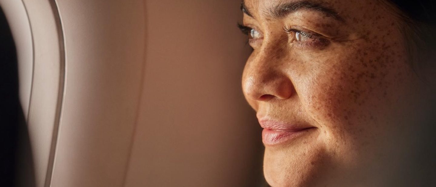 A woman looks thoughtfully out of an aeroplane window.