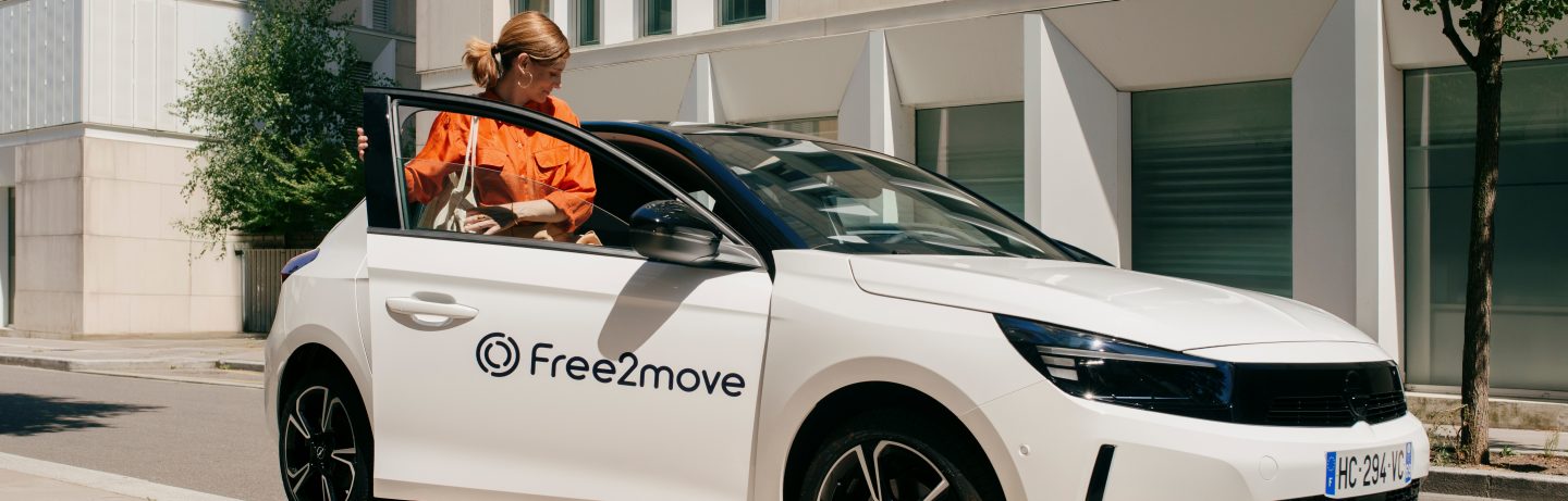 A couple leans against a Free2move car and takes a selfie.