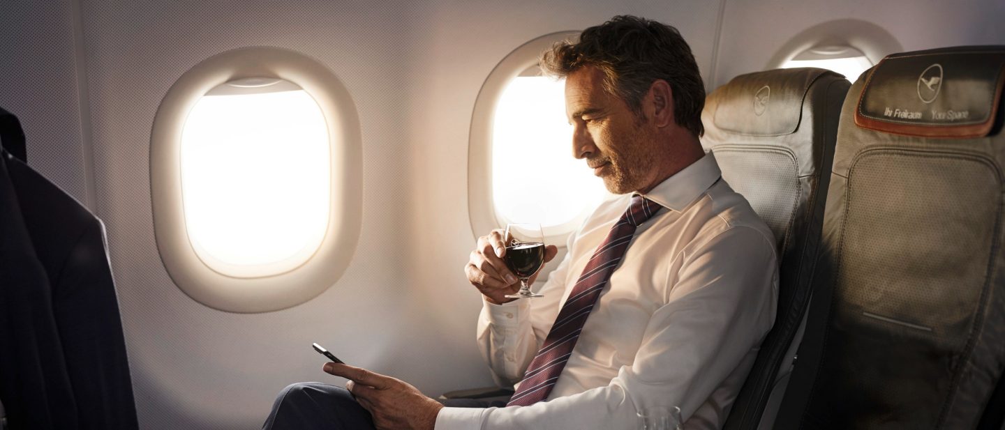 Man drinking wine and looking at his mobile phone in Business Class