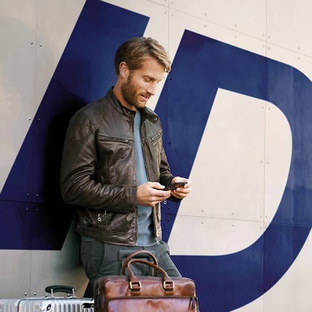 A man with a suitcase looking at his phone in front of a large "ID" logo.